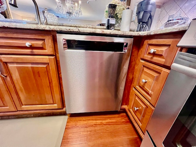 details with light hardwood / wood-style flooring, stainless steel dishwasher, light stone counters, and an inviting chandelier