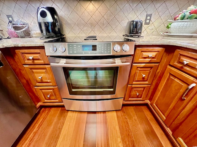 kitchen featuring backsplash, stainless steel range, light stone countertops, and light hardwood / wood-style flooring