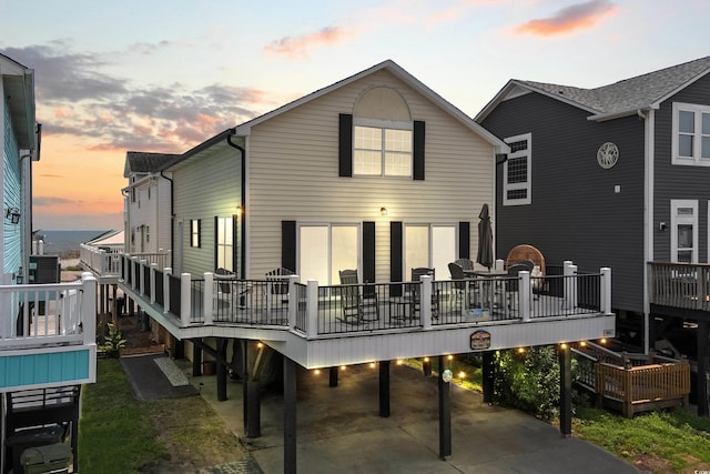 back house at dusk with a wooden deck and a carport