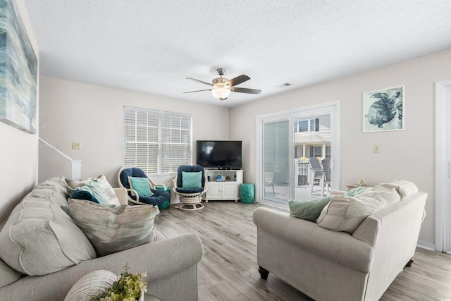 living room featuring ceiling fan, light hardwood / wood-style flooring, and a textured ceiling