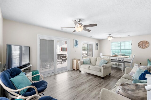 living room with ceiling fan, a textured ceiling, and light hardwood / wood-style floors