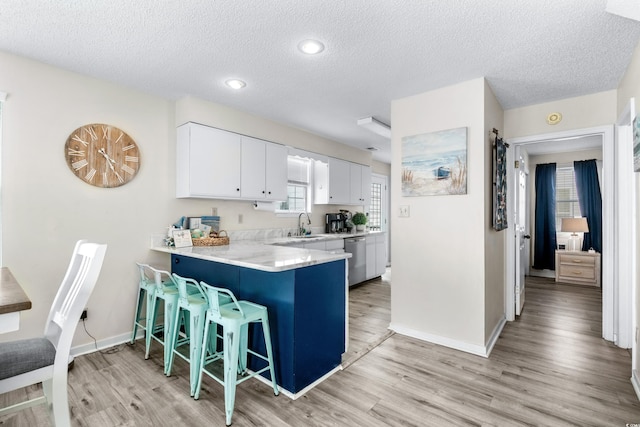 kitchen featuring white cabinets, dishwasher, a kitchen bar, light hardwood / wood-style floors, and kitchen peninsula