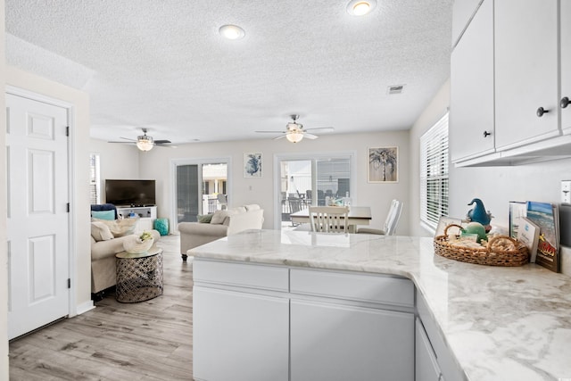 kitchen featuring white cabinetry, light hardwood / wood-style flooring, light stone countertops, and a textured ceiling