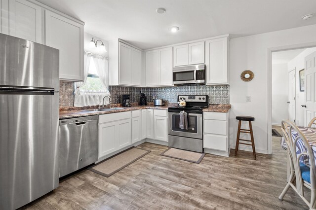 kitchen featuring hardwood / wood-style flooring, tasteful backsplash, white cabinetry, appliances with stainless steel finishes, and sink