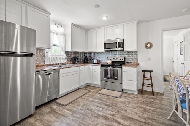 kitchen with tasteful backsplash, appliances with stainless steel finishes, light wood-style flooring, and a sink