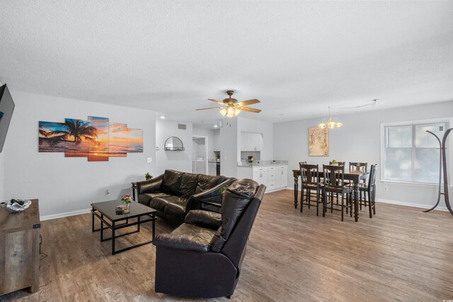 living room with a textured ceiling, ceiling fan with notable chandelier, and light wood-type flooring