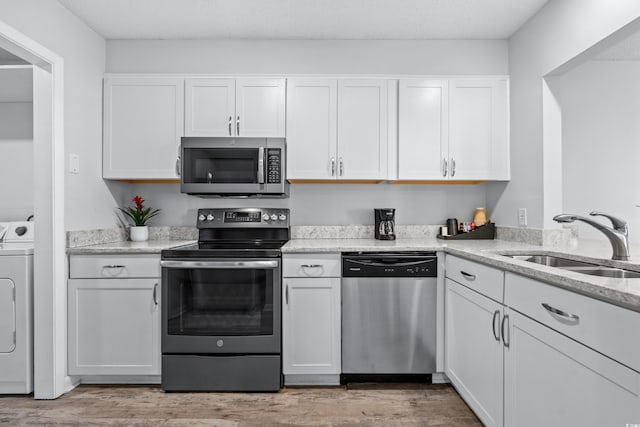 kitchen with washer / clothes dryer, appliances with stainless steel finishes, white cabinetry, light wood-type flooring, and sink