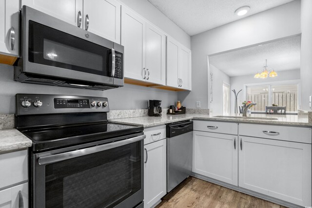 kitchen with a textured ceiling, stainless steel appliances, white cabinets, a notable chandelier, and light hardwood / wood-style flooring