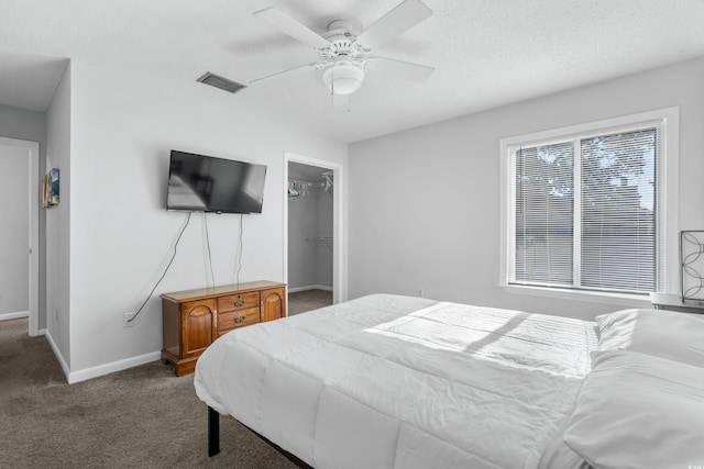 bedroom with ceiling fan, a textured ceiling, carpet flooring, a closet, and a walk in closet