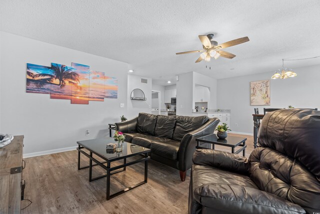 living room featuring a textured ceiling, wood-type flooring, and ceiling fan with notable chandelier