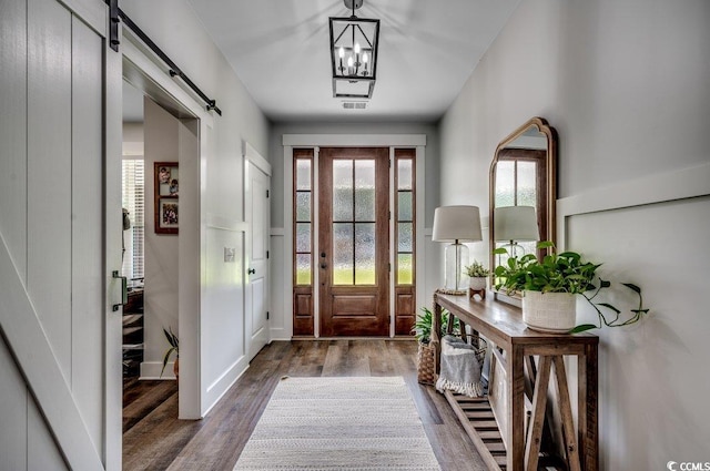 foyer with a barn door, dark wood-type flooring, and an inviting chandelier