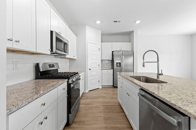 kitchen featuring light stone counters, light hardwood / wood-style floors, sink, white cabinetry, and appliances with stainless steel finishes