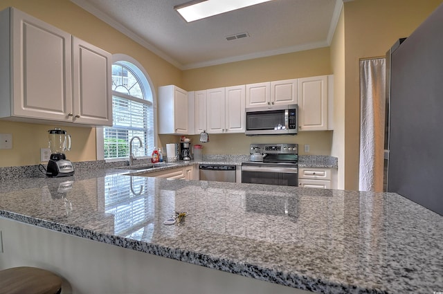 kitchen with stainless steel appliances, white cabinets, sink, stone counters, and kitchen peninsula