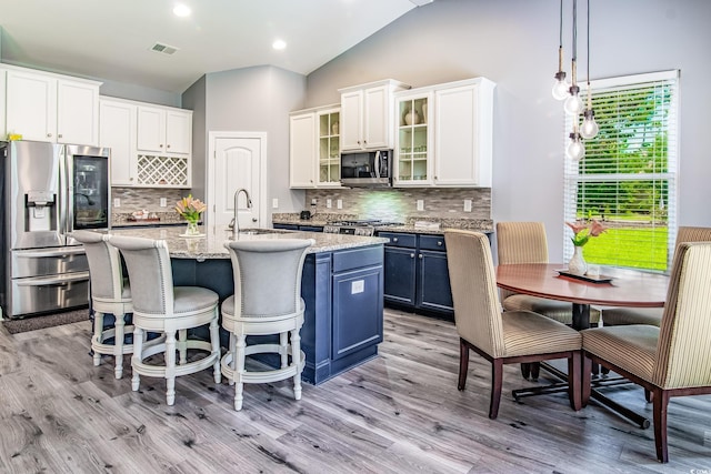 kitchen with blue cabinets, pendant lighting, stainless steel appliances, and a center island with sink