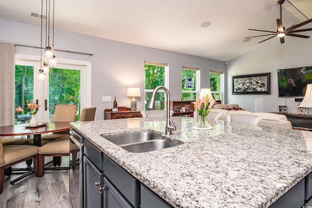 kitchen featuring light stone counters, an island with sink, sink, and hanging light fixtures