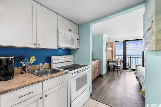 kitchen featuring floor to ceiling windows, sink, white cabinetry, light wood-type flooring, and white appliances