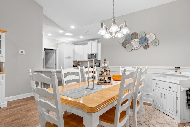 dining room featuring light wood-type flooring, vaulted ceiling, and an inviting chandelier