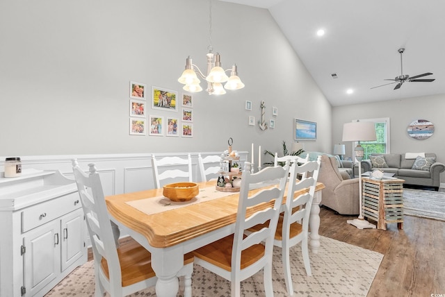 dining space with high vaulted ceiling, wood-type flooring, and ceiling fan with notable chandelier