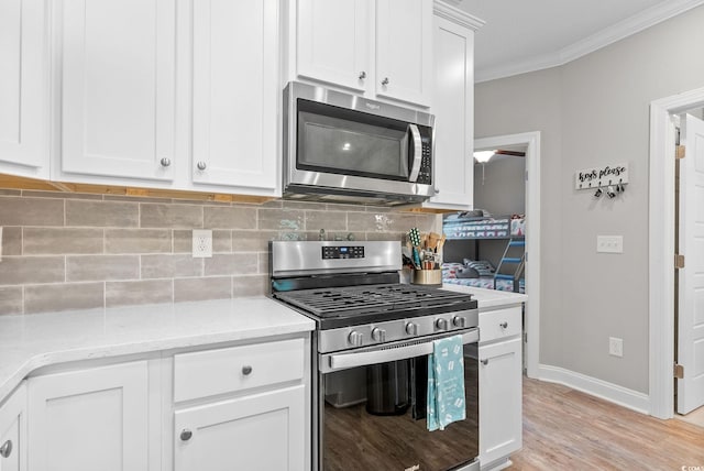 kitchen with light hardwood / wood-style flooring, light stone counters, appliances with stainless steel finishes, white cabinets, and tasteful backsplash