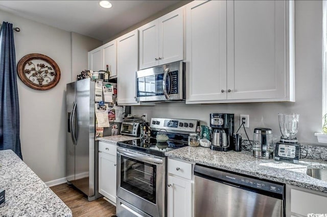 kitchen featuring appliances with stainless steel finishes, light hardwood / wood-style floors, light stone counters, and white cabinets