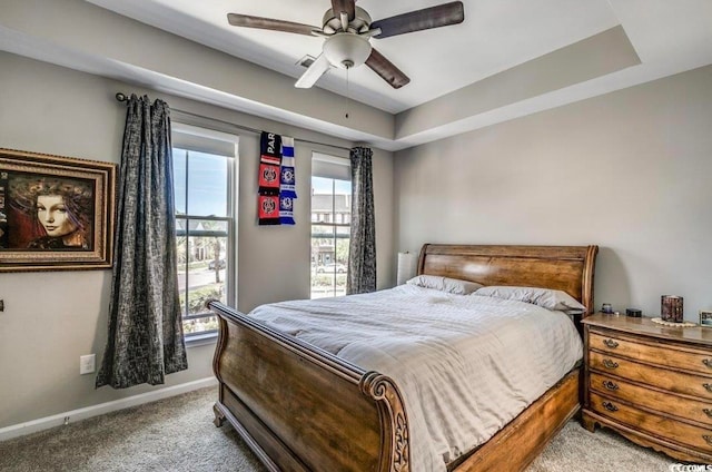 bedroom featuring a raised ceiling, ceiling fan, and light colored carpet