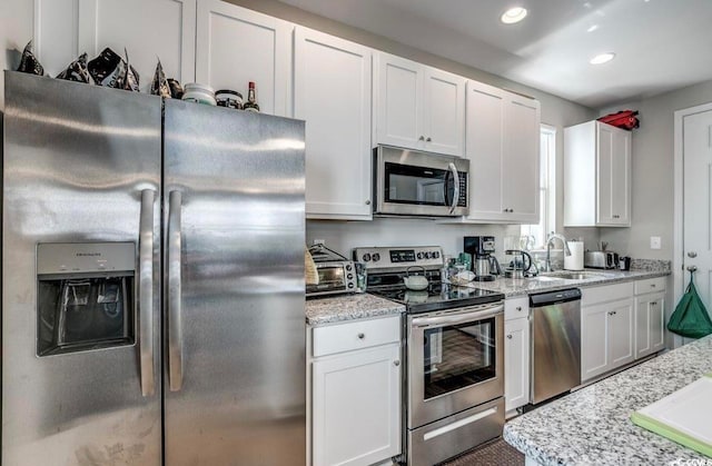 kitchen featuring appliances with stainless steel finishes, white cabinetry, sink, and light stone counters