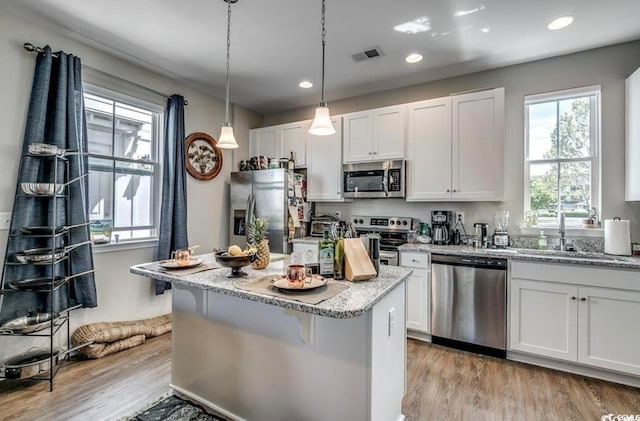 kitchen with light wood-type flooring, white cabinetry, a kitchen island, appliances with stainless steel finishes, and light stone countertops