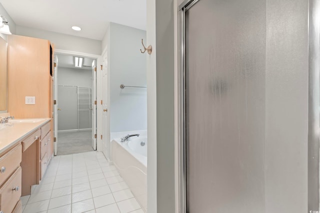 bathroom featuring tile patterned flooring, a relaxing tiled tub, and vanity