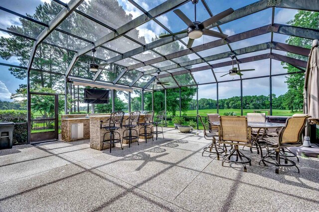 view of patio featuring ceiling fan, an outdoor bar, exterior kitchen, and a lanai