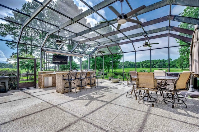 view of patio with a bar, ceiling fan, and glass enclosure