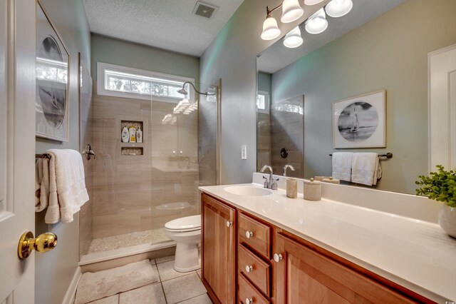 bathroom with a textured ceiling, toilet, vanity, a tile shower, and tile patterned flooring