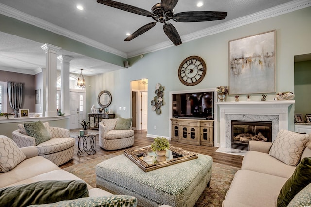 living room featuring a high end fireplace, decorative columns, ornamental molding, hardwood / wood-style flooring, and ceiling fan