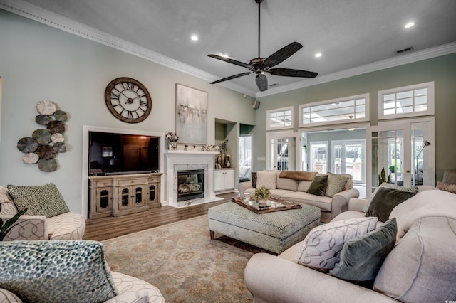 living room featuring crown molding, a towering ceiling, hardwood / wood-style flooring, ceiling fan, and a high end fireplace