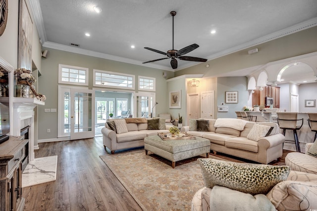 living room featuring crown molding, ceiling fan, a high ceiling, a high end fireplace, and light wood-type flooring