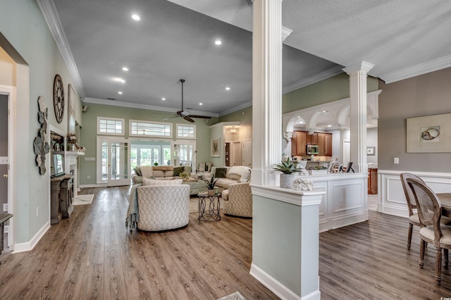 living room with crown molding, a textured ceiling, ceiling fan, ornate columns, and light hardwood / wood-style flooring