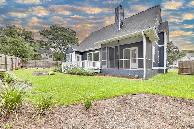 back house at dusk with a sunroom and a yard