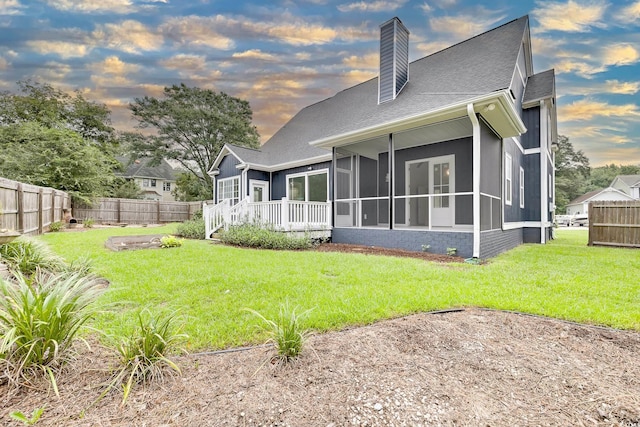 back of property with a sunroom, a fenced backyard, a chimney, and a yard