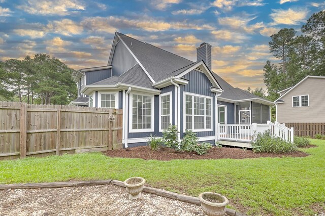 back house at dusk with a sunroom and a yard