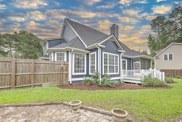 rear view of property featuring a wooden deck, a chimney, fence, and a sunroom