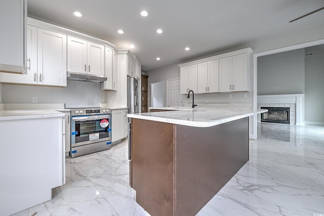 kitchen featuring appliances with stainless steel finishes, light tile patterned floors, a tiled fireplace, and white cabinetry