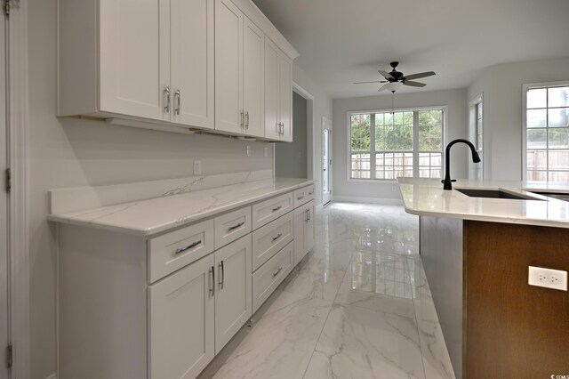 kitchen with light tile patterned floors, an island with sink, ceiling fan, sink, and white cabinetry