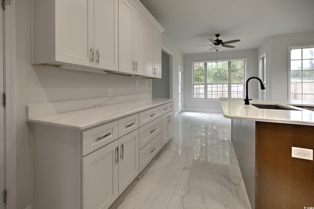 kitchen featuring an island with sink, light stone counters, marble finish floor, white cabinetry, and a sink