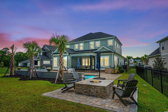 back house at dusk with a lawn, a patio, and an outdoor fire pit