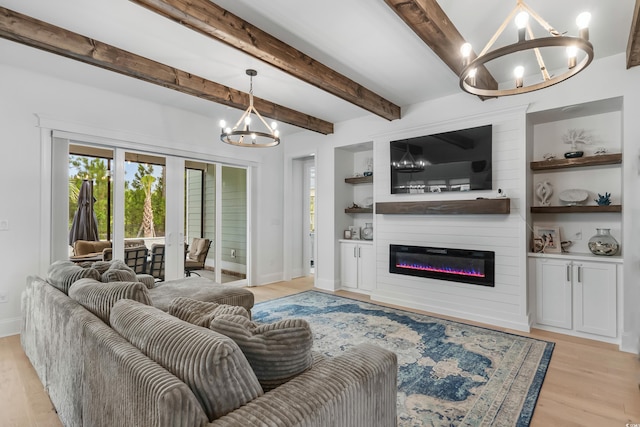 living room featuring built in shelves, light wood-type flooring, a large fireplace, a notable chandelier, and beamed ceiling