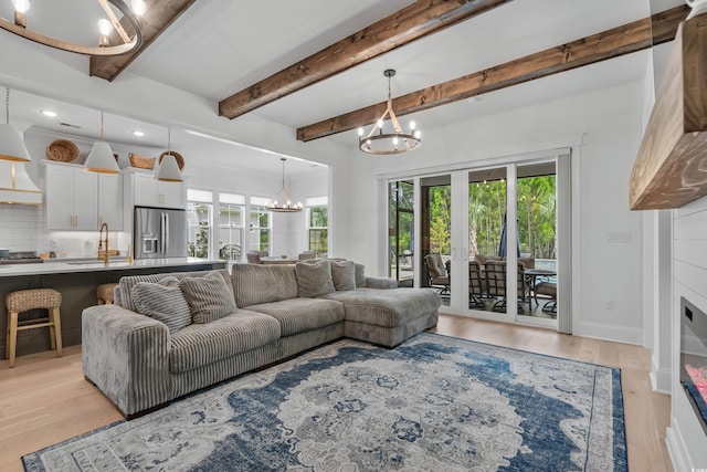 living room featuring an inviting chandelier, sink, a wealth of natural light, and light hardwood / wood-style floors