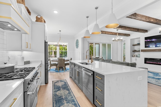 kitchen with appliances with stainless steel finishes, white cabinetry, sink, a kitchen island with sink, and custom range hood