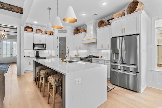 kitchen featuring a center island with sink, stainless steel appliances, custom range hood, and white cabinets