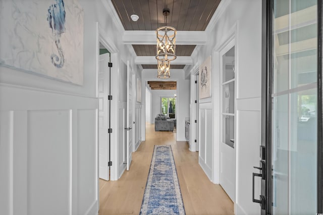 corridor with beamed ceiling, ornamental molding, a notable chandelier, wood ceiling, and light wood-type flooring