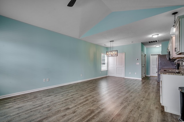 interior space featuring sink, pendant lighting, wood-type flooring, dark stone counters, and vaulted ceiling