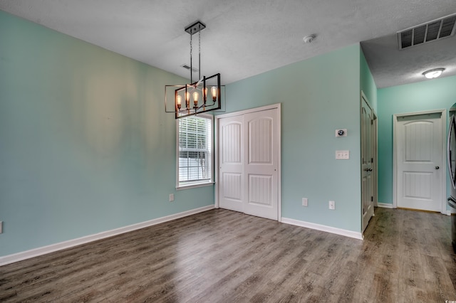 unfurnished dining area with a textured ceiling, a chandelier, and wood-type flooring